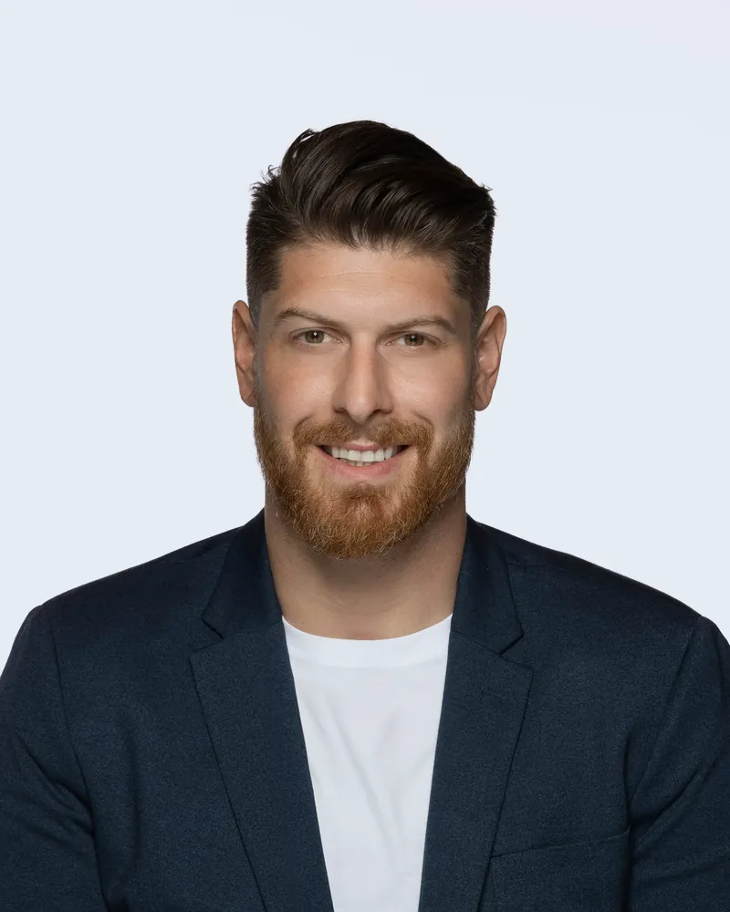 Portrait de Francis Lauzon, fondateur de Voltige services comptables, souriant, en veston bleu marine et t-shirt blanc